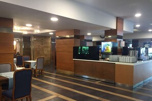 A modern restaurant with a central counter, seating area, and a large screen displaying content.
