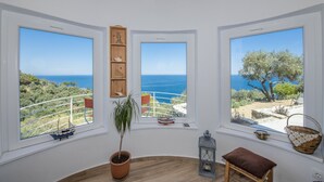 A room with three large windows overlooking a coastal landscape, a wooden ceiling, a potted plant, a small table, and a lantern. - Villa Avgi (Sunrise & Pool Sea View Area) (Skopelos)