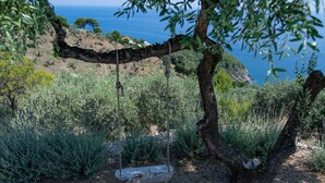 A secluded outdoor seating area with two wooden lounge chairs under a tree, overlooking a coastal landscape. - Villa Avgi (Sunrise & Pool Sea View Area) (Skopelos)