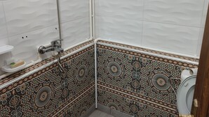 Un baño con ducha, inodoro y lavamanos. Las paredes están cubiertas de azulejos blancos con un diseño decorativo.