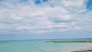A beach with a pier extending into the water, a lighthouse, and a clear sky. - Le Panoramic - 180° sea view & port - Balcony - Elevator - Garage - Waterfront (Grandcamp-Maisy)