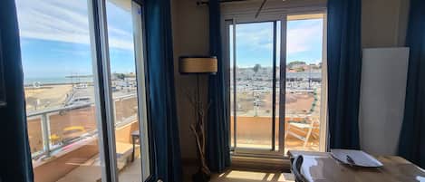 Ein Zimmer mit großem Fenster mit Blick auf eine Marina und Gebäude, einer Stehlampe und einem Tisch mit Teller und Tasse.