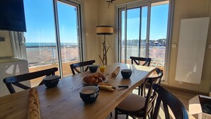 A dining area with a wooden table, chairs, and breakfast items. - Le Panoramic - 180° sea view & port - Balcony - Elevator - Garage - Waterfront (Grandcamp-Maisy)