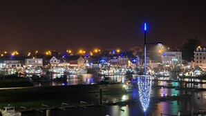 A nighttime harbor scene with boats docked, illuminated by various lights. - Le Panoramic - 180° sea view & port - Balcony - Elevator - Garage - Waterfront (Grandcamp-Maisy)