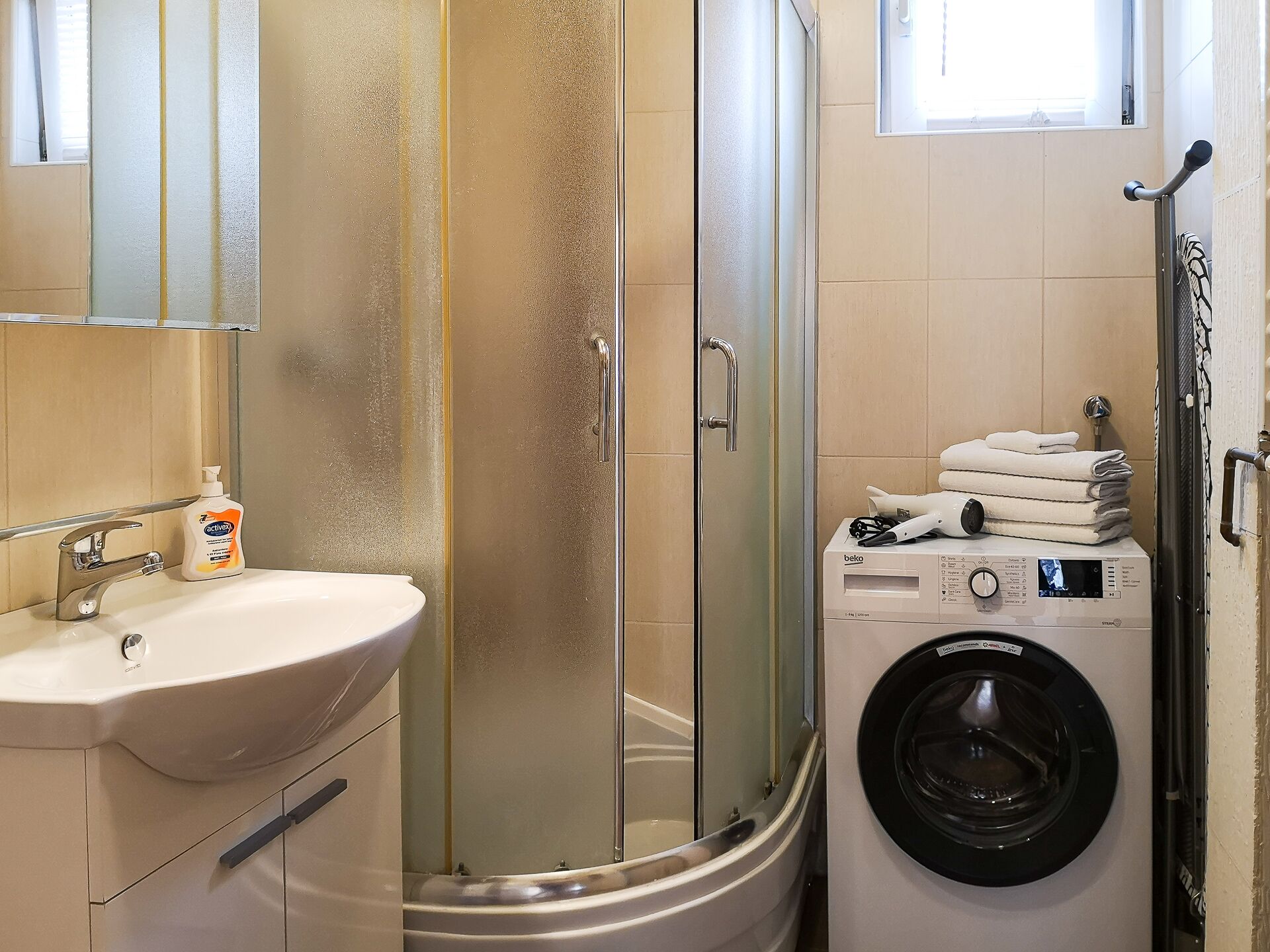 A bathroom with a sink, a glass shower enclosure, and a front-loading washing machine.