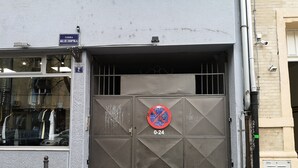 Une grille métallique recouverte de graffitis, une enseigne bleue au-dessus, et une vitrine où sont exposés des vêtements.