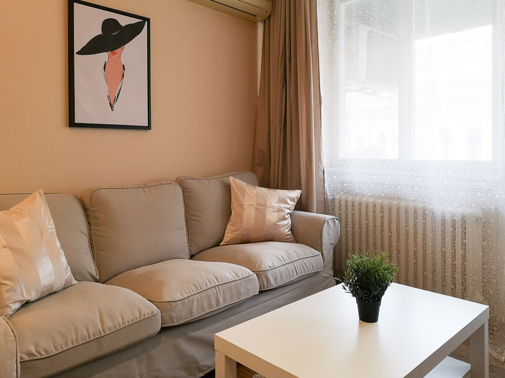 A living room with a beige sofa, a white coffee table, and a framed artwork on the wall.