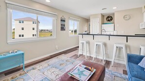 A spacious living area with a large window, a kitchen with a bar, and a blue sofa.