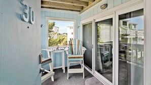 A balcony with a view of a residential area, featuring a wooden ceiling, a sliding glass door, and two chairs.
