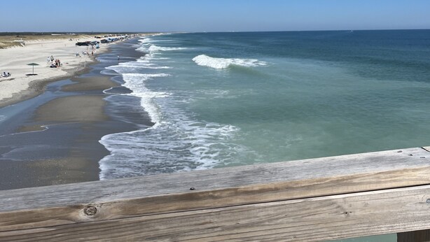 A wooden deck overlooking a beach with waves and a clear blue sky.