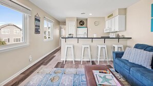 A modern kitchen with white cabinets, a central island with bar stools, and a view of neighboring houses.