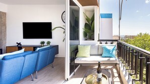 Un balcon avec un canapé, une table avec une bouteille et des verres, une télévision et une plante.