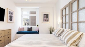 Une chambre à coucher avec un grand lit, une fenêtre avec des stores, une table de chevet et une commode.