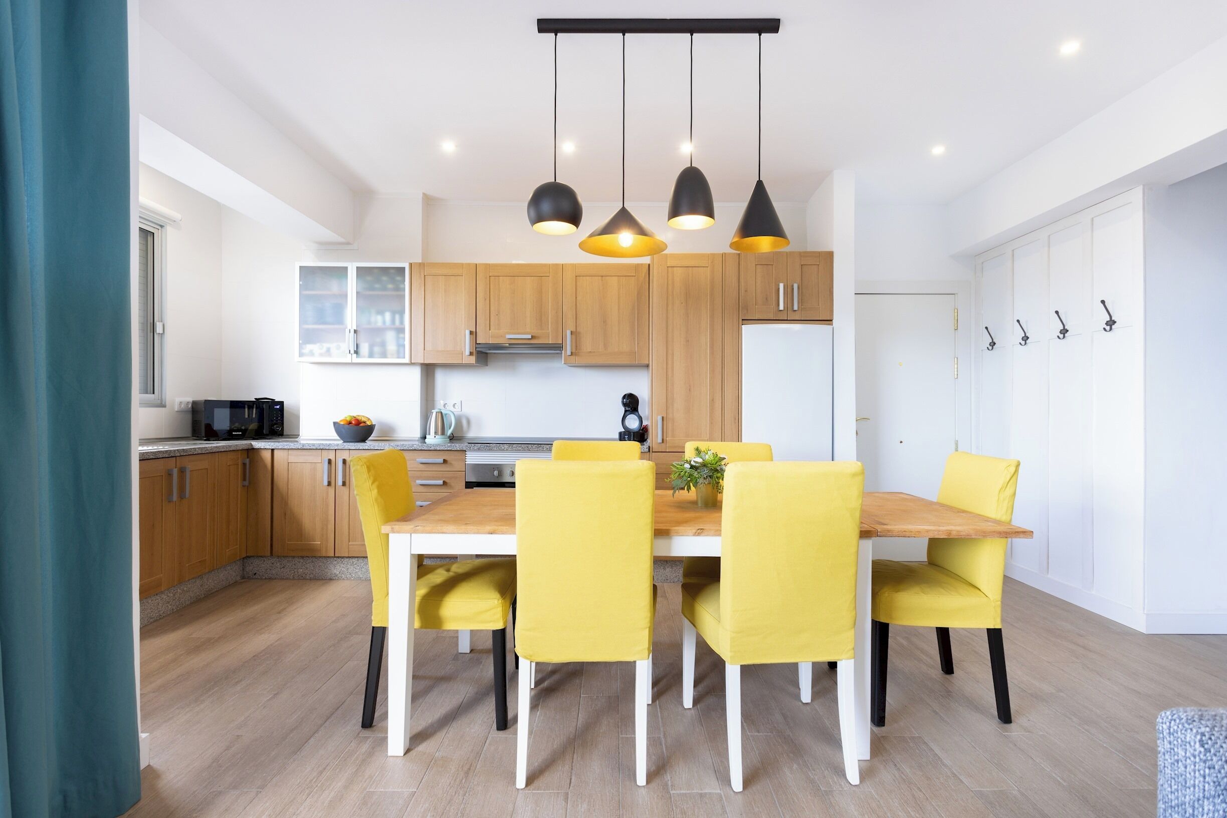 Una cocina moderna con armarios de madera, un refrigerador blanco y una mesa de comedor con sillas amarillas.