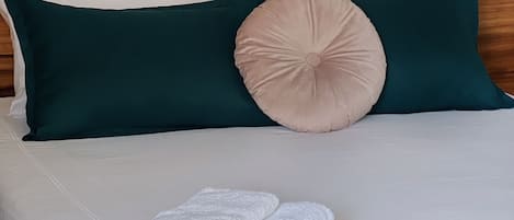 Una cama bien hecha con sábanas blancas, almohadas verde azulado y oscuro, y una manta verde azulado.