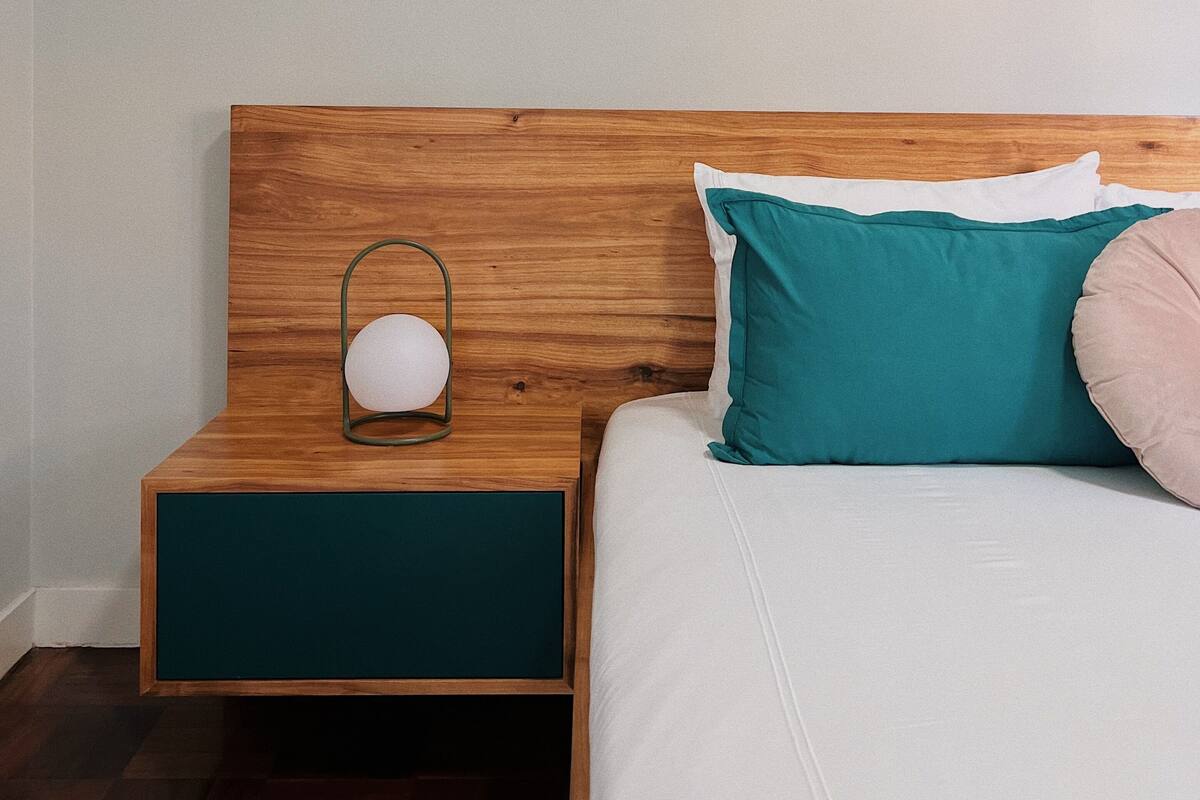 A bedroom with a wooden headboard, a bedside table with a lamp, and a bed with teal and white pillows.