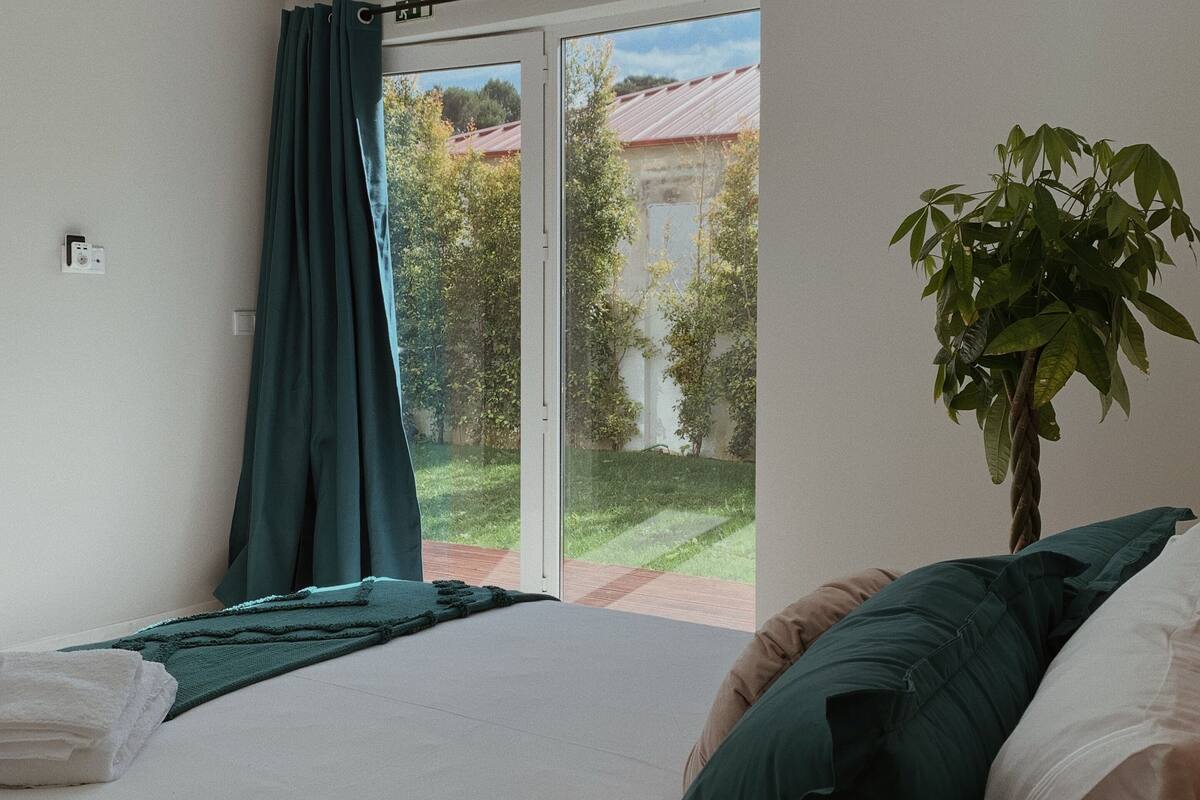 A bedroom with a bed, a plant, and a view of a building through a glass door.