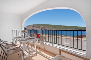 Un balcón con una mesa dispuesta para comer, sillas y vistas al mar y acantilados.