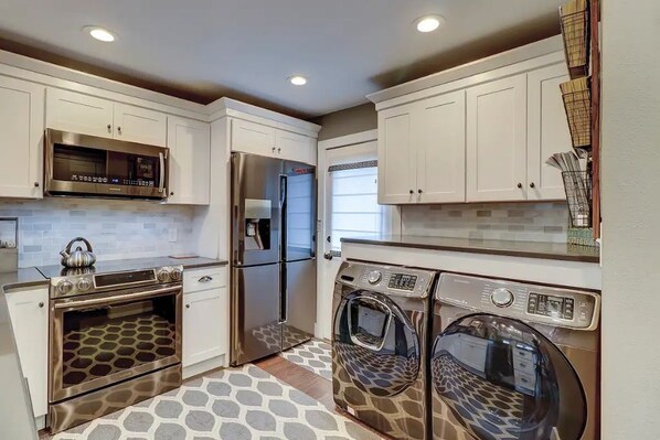 Una cocina compacta con electrodomésticos de acero inoxidable, muebles de cocina blancos y piso estampado.