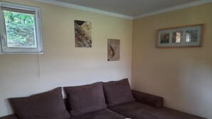Een kamer met een bruine bank, een klein houten tafeltje en drie kunstwerken in lijsten aan de muur.