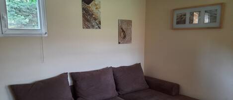 A room with a brown sofa, a small wooden table, and three framed artworks on the wall.