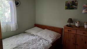 Een enkel bed met witte beddengoed, een houten hoofdbord, een nachtkastje met een lamp en een klein kastje.
