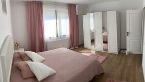 Ein Schlafzimmer mit einem Bett, rosa Vorhängen, einem Heizkörper und einem Kleiderschrank.