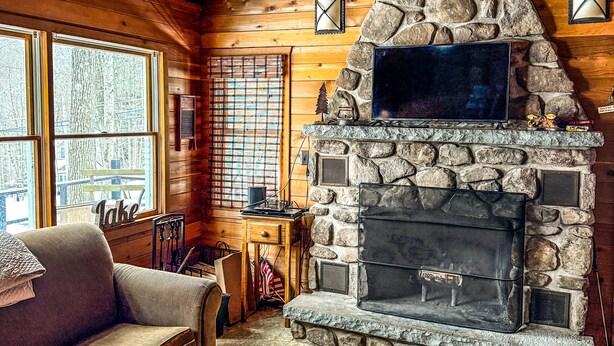 Interior acogedor de una cabaña con chimenea de piedra, vigas de madera y un sofá.
