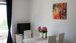 A dining area with a white table, four chairs, a vase with pink flowers, a painting on the wall, and a television on a stand. - Apartment in Vodice with Seaview, Balcony, Air condition, WIFI (612-4) (Vodice)