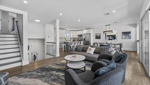 A spacious living area with a grey sofa, a coffee table, and a staircase leading to an upper level. - Waterfront Firepit Game Room at Legacy Beach House (Point Pleasant Beach)