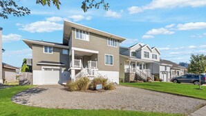 A two-story residential building with a front porch, a driveway, and a well-maintained lawn. - Waterfront Firepit Game Room at Legacy Beach House (Point Pleasant Beach)