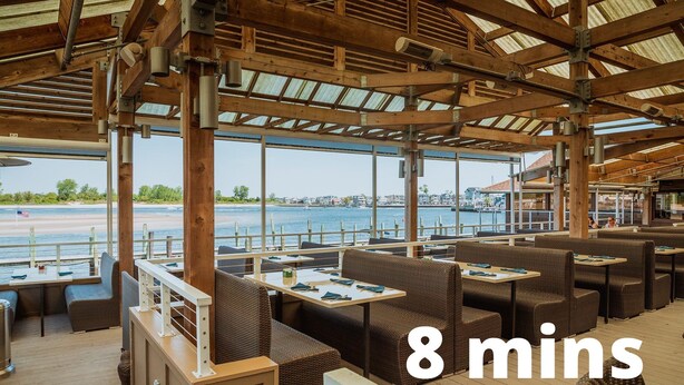 An outdoor restaurant with wooden beams, wicker furniture, and a view of the water. - Waterfront Firepit Game Room at Legacy Beach House (Point Pleasant Beach)