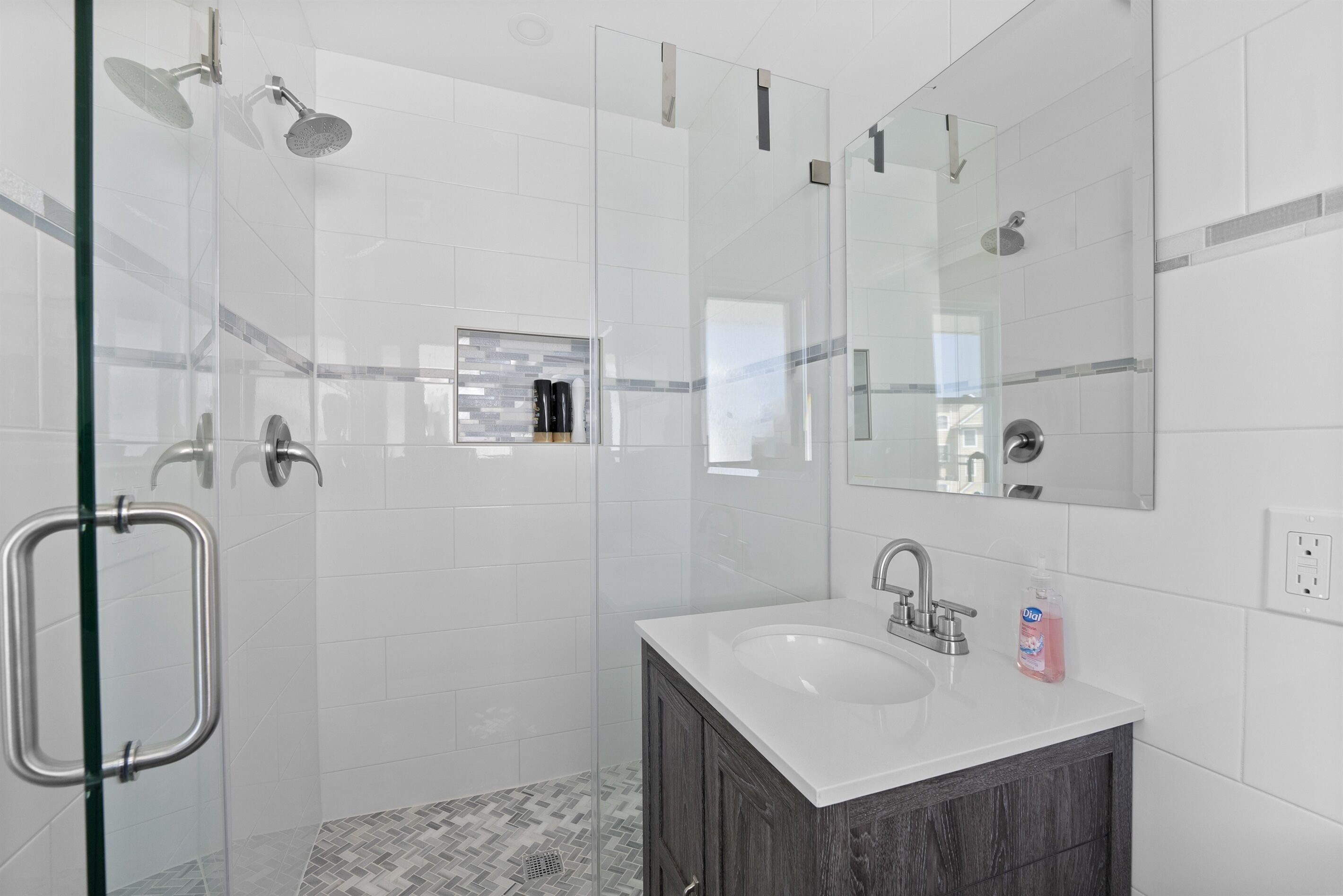 Un baño moderno con cabina de ducha de vidrio, lavamanos blanco y mueble de tocador de madera oscura.