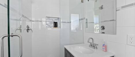 Un baño moderno con cabina de ducha de vidrio, lavamanos blanco y mueble de tocador de madera oscura.