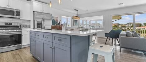 A modern kitchen with grey cabinets, stainless steel appliances, and pendant lighting.