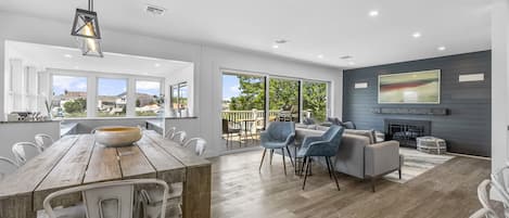 A spacious living area with a wooden dining table, modern chairs, a grey sofa, and a fireplace.
