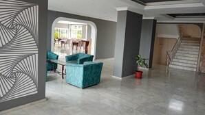 A spacious interior with a dining area, teal armchairs, a staircase, and a geometric wall design. - Moonstar Hotel (Kusadasi)