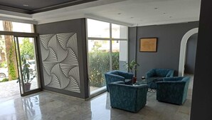 A modern lobby with a geometric wall design, two blue armchairs, a glass coffee table, and a potted plant. - Moonstar Hotel (Kusadasi)