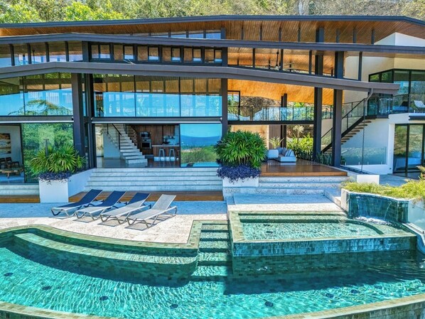 Une maison moderne dotée d’une piscine, d’un espace salon extérieur et d’un escalier menant à une terrasse.