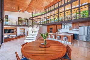 Una cocina moderna y espaciosa con una isla central, un comedor con una mesa redonda de madera y una escalera que conduce a un nivel superior.