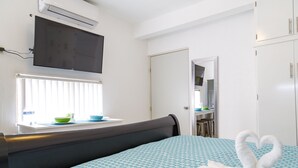 Ein Hotelzimmer mit Bett, Wandfernseher, Fenster mit Jalousien, Spiegel und Kleiderschrank.