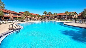 A large, clear swimming pool with lounge chairs and palm trees, surrounded by multi-story buildings with red roofs. - Cozy 2-bedroom stay with great amenities (Panama City Beach)
