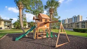 A playground with a wooden playhouse, a slide, and swings. - Cozy 2-bedroom stay with great amenities (Panama City Beach)