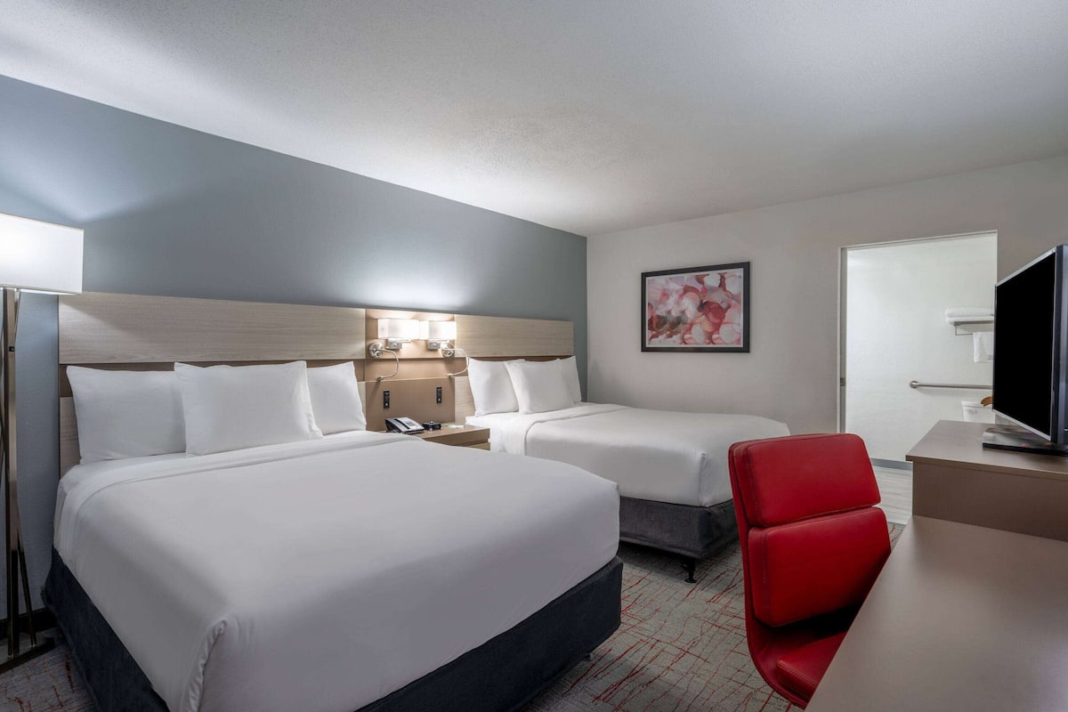 A hotel room with two beds, a desk, a TV, and a red chair.