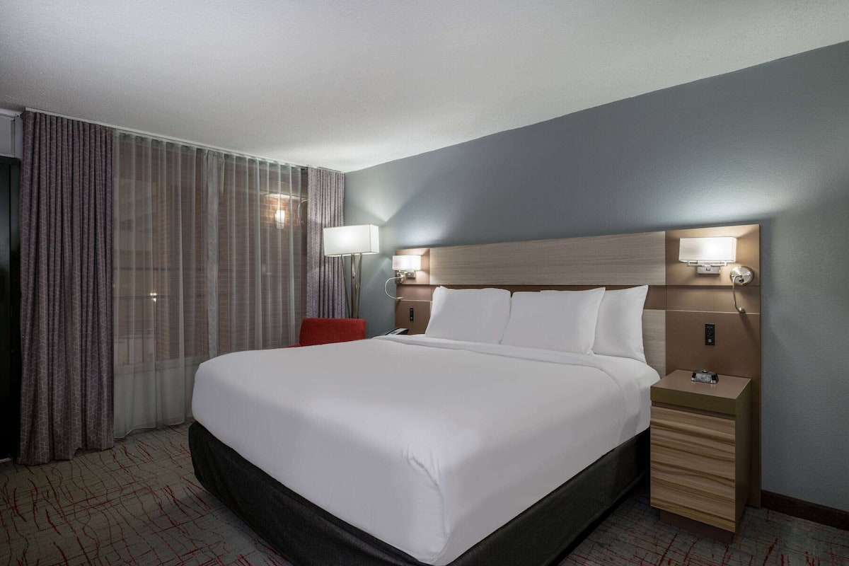 A hotel room with a large bed, two bedside lamps, a nightstand, and a red chair.