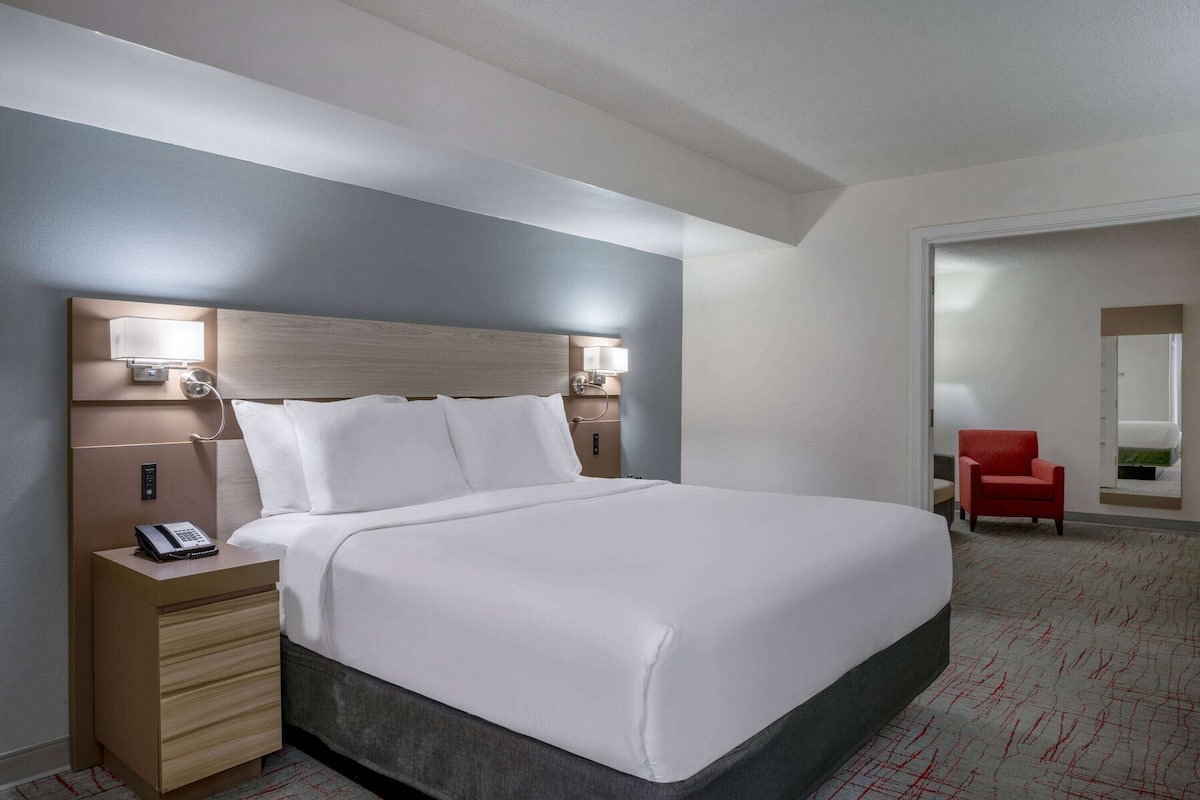 A hotel room with a large bed, bedside lamps, a telephone on the nightstand, and a red chair in the corner.