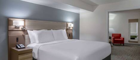 Habitación de hotel con una cama grande, lámparas de noche, un teléfono en la mesita y una silla roja en la esquina.