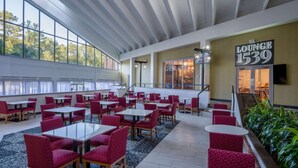 A spacious lounge area with multiple seating arrangements, a staircase leading to an upper level, and a large window providing natural light.