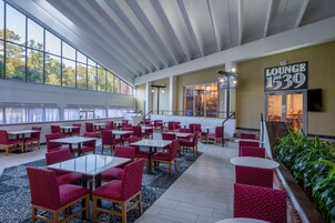 A spacious lounge area with multiple seating arrangements, a staircase leading to an upper level, and a large window providing natural light.