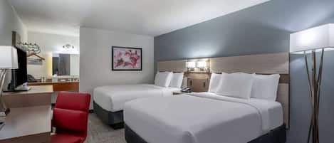 A hotel room with two beds, a desk, a chair, a desk lamp, a bedside table, and a wall-mounted TV.